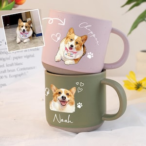 以下が含まれることがあります： ピンクとグリーンの2つのセラミックマグが積み重ねられています。ピンクのマグには、"Happy Birthday"のよだれかけと"Chopper"という名前のコーギーのイラストが描かれています。グリーンのマグには、コーギーのイラストと"Noah"という名前が描かれています。