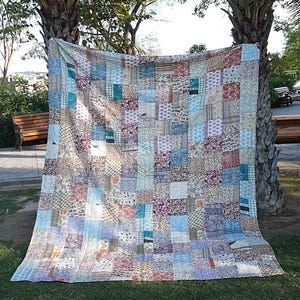 May include: A patchwork quilt with a variety of colors and patterns, including blue, brown, purple, and white. The quilt is made of many different fabrics sewn together in a random pattern.