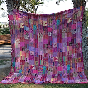 Può includere: Una trapunta patchwork realizzata con ritagli di tessuto colorati in tonalità di rosa, viola e blu. La trapunta è realizzata in uno stile tradizionale con una varietà di motivi e texture.
