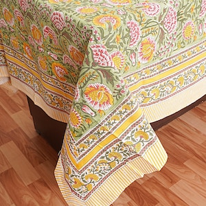 May include: A green tablecloth with a floral pattern in shades of yellow, pink, and green. The tablecloth has a yellow and white border with a striped pattern.