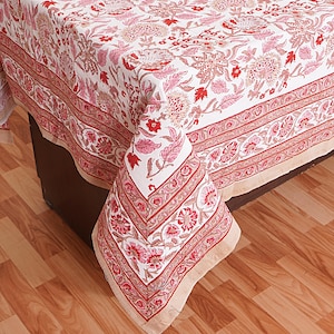 May include: A white tablecloth with a red and pink floral pattern. The tablecloth has a border with a repeating pattern of red and white stripes.