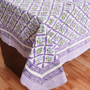 May include: A white tablecloth with a purple and green floral pattern. The tablecloth has a border with a striped pattern and a floral design.