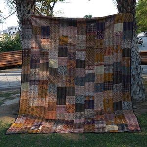 Op de afbeelding: Een patchworkdeken met verschillende kleuren en patronen, waaronder bruin, beige, blauw en paars. De deken is gemaakt van verschillende stoffen die in een willekeurig patroon aan elkaar zijn genaaid.