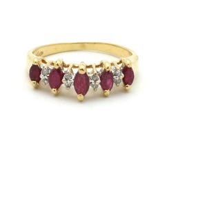 May include: A gold ring featuring a row of marquise-cut, deep red gemstones alternating with small, round, clear gemstones. The ring is set against a white background, highlighting the jewelry's design and color.