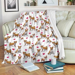 May include: White throw blanket featuring a repeating pattern of brown and white dogs and red hearts. The blanket is draped over a sofa, creating a cozy and decorative accent for the living space.