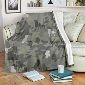 Può includere: Una coperta grigia mimetica con sagome di cani in varie pose. La coperta ha un retro bianco ed è drappeggiata su un divano. Le sagome dei cani sono in tonalità di grigio e bianco.