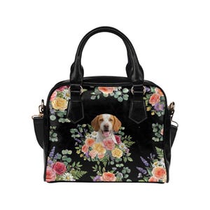 May include: Black handbag featuring a dog surrounded by a floral arrangement of roses, daisies, and lavender. The bag has a top handle and a detachable shoulder strap. The bag's exterior is black with a floral pattern.