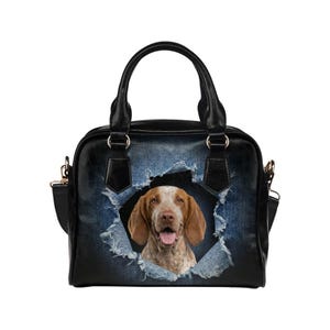 May include: Black handbag with a distressed denim design featuring a brown and white dog. The bag has a top handle, a shoulder strap, and gold-colored hardware. The dog's face is visible through a torn denim effect.