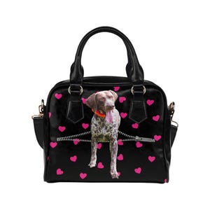 May include: Black handbag with pink hearts and a dog graphic. The dog appears to be emerging from a zipper. The bag has a top handle and a shoulder strap.