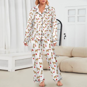 May include: White pajama set with a repeating pattern of brown dogs and red hearts. The long-sleeved top and pants have black trim. The pajamas are made of a silky material.