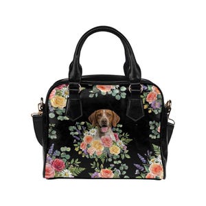 May include: Black handbag with a floral pattern and a dog portrait. The bag features a top handle and a shoulder strap. The floral design includes roses, daisies, and other flowers in shades of pink, yellow, and orange.