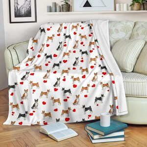 May include: White throw blanket featuring a repeating pattern of Basenji dogs in various poses, interspersed with red hearts. The dogs are in shades of black, brown, and tan. The blanket is draped over a sofa.