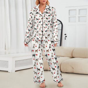 May include: White pajama set with a repeating pattern of dogs and red hearts. The long-sleeved top has black trim and buttons. The matching pants also have black trim at the ankles. The pajamas are made of a silky material.
