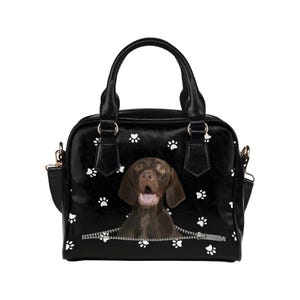 May include: Black handbag with a brown dog graphic emerging from a zipper. The bag features white paw prints and a top handle. Includes a detachable shoulder strap and gold-colored hardware.