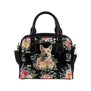 Puede incluir: Bolso de mano negro con estampado floral y retrato de perro. El bolso presenta un perro sonriente rodeado de rosas, margaritas y otras flores. Tiene asas negras y una correa para el hombro.