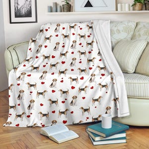 Può includere: Coperta bianca con un motivo ripetuto di cani beagle e cuori rossi. La coperta è drappeggiata su un divano ed è realizzata in un materiale morbido e accogliente. I cani beagle sono in varie pose.