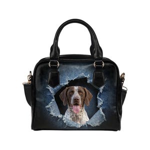 May include: Black handbag with a dog graphic. The bag features a distressed denim design with a torn-out section revealing a German Shorthaired Pointer. The bag has black handles and a shoulder strap.