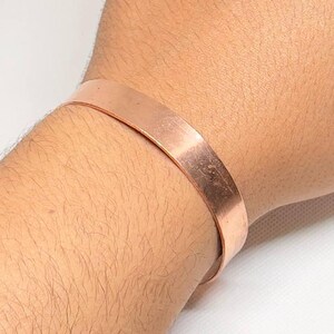 May include: A simple copper bracelet with a smooth, polished finish. The bracelet is worn on a person's wrist.