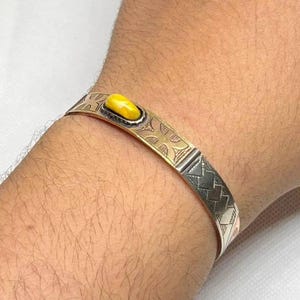 May include: A silver and gold bracelet with a yellow stone set in the center. The bracelet has a geometric design.