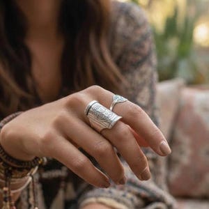 Peut inclure: Ensemble de bagues en argent comprenant deux bagues. La plus grande bague a un motif gravé et une forme rectangulaire. La plus petite bague a une forme triangulaire. Les bagues sont portées sur une main.