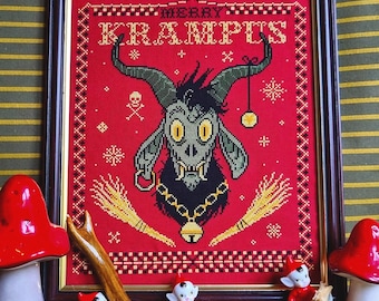 May include: Framed cross-stitch art with a red background and the words "MERRY KRAMPUS". The artwork features a horned goat-like figure with a bell necklace, surrounded by decorative elements. Miniature figurines and mushrooms are in the foreground.