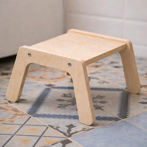 Peut inclure: Un petit marchepied en bois clair avec un dessus rectangulaire et quatre pieds inclinés. Le tabouret est en bois non fini et est fixé avec des vis métalliques. Le design est simple et fonctionnel, adapté à divers usages.