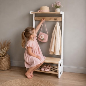 Könnte beinhalten: Eine Kindergarderobe aus hellem Holz und Weiß mit einer oberen Ablage, einer Kleiderstange mit Haken und einem unteren Schuhregal. Das Möbelstück verfügt über eine natürliche Holzoberfläche auf den horizontalen Ebenen und weiße Seitenwände.