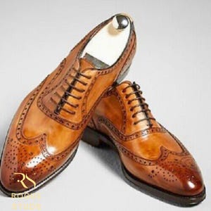 May include: A pair of brown leather dress shoes with intricate brogue detailing. The shoes feature a classic lace-up design and a polished finish. The image showcases the shoes from a slightly elevated angle, highlighting their craftsmanship.