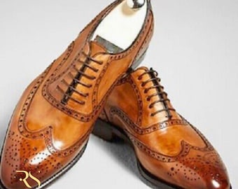 May include: A pair of brown leather dress shoes with intricate brogue detailing. The shoes feature a classic lace-up design and a polished finish. The image showcases the shoes from a slightly elevated angle, highlighting their craftsmanship.