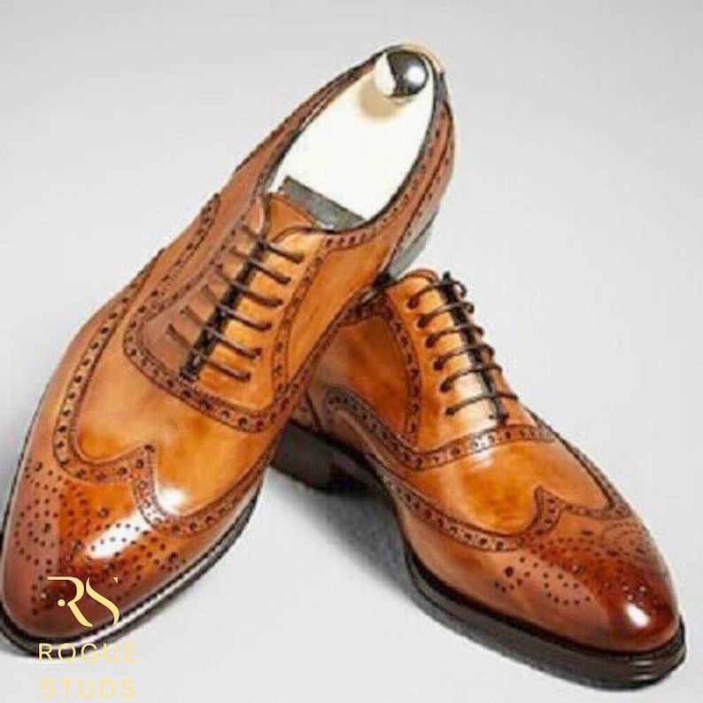 May include: A pair of brown leather dress shoes with intricate brogue detailing. The shoes feature a classic lace-up design and a polished finish. The image showcases the shoes from a slightly elevated angle, highlighting their craftsmanship.