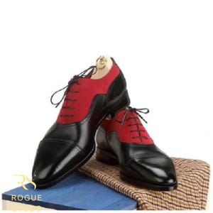 May include: A pair of two-tone dress shoes. The shoes are black with red suede panels on the upper. The shoes have black laces and are displayed on a blue surface with a patterned cloth.
