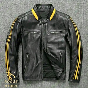 Könnte beinhalten: Schwarze Lederjacke mit gelben Rennstreifen an Ärmeln und Kragen. Die Jacke hat einen Reißverschluss vorne, zwei Reißverschlusstaschen und den Text "ROGUE STUDS" unten links.