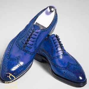 May include: A pair of blue leather dress shoes with brogue detailing and black laces. The shoes have a glossy finish and are displayed on a white surface. The shoes are a classic style.