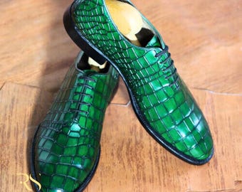 May include: A pair of green leather dress shoes with a crocodile skin pattern. The shoes have black laces and soles. The logo "ROGUE STUDS" is visible in the lower left corner.