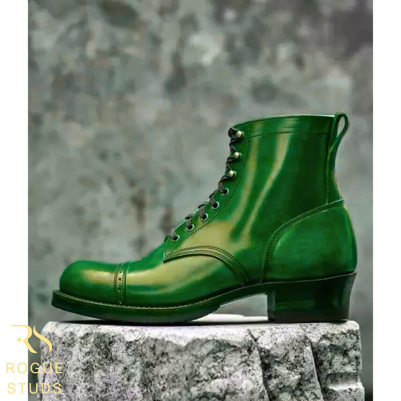 May include: A single, glossy green leather boot with a cap toe and lace-up closure. The boot has a stacked heel and a pull tab at the top. The boot is displayed on a textured stone surface.