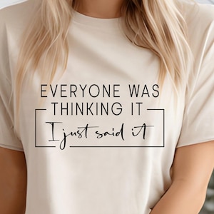 May include: A cream-colored t-shirt with the text "EVERYONE WAS THINKING IT - I just said it" in black. The text is centered and framed by a black rectangle. The shirt is short-sleeved.