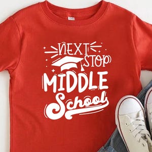 May include: A red t-shirt with the text "NEXT STOP MIDDLE SCHOOL" in white, paired with denim shorts and white sneakers. The shirt features a graduation cap graphic, perfect for back-to-school or graduation.