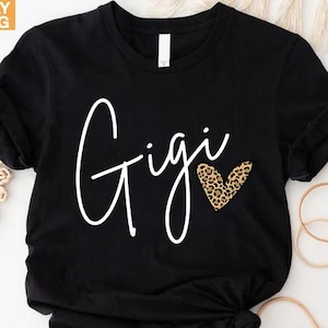 May include: Black t-shirt with white text that says 'Gigi' and a heart with a leopard print pattern.