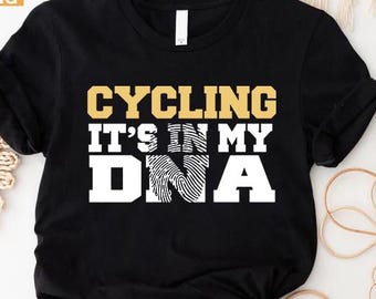 May include: Black t-shirt with the text "CYCLING IT'S IN MY DNA" in gold and white. The design incorporates a fingerprint graphic within the word "DNA". The shirt is from Custom Trendy Shirts.