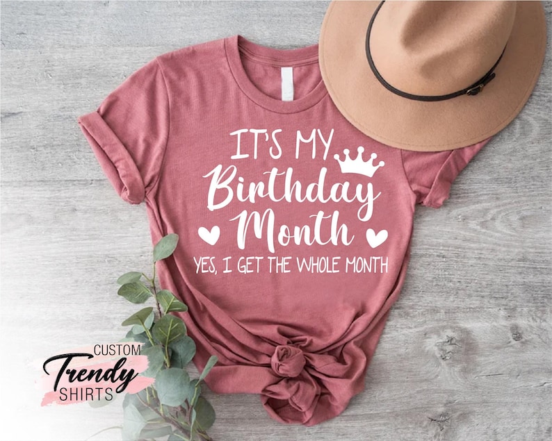 May include: A pink t-shirt with the text "It's My Birthday Month" and a crown graphic. The text "Yes, I get the whole month" is below the main text.