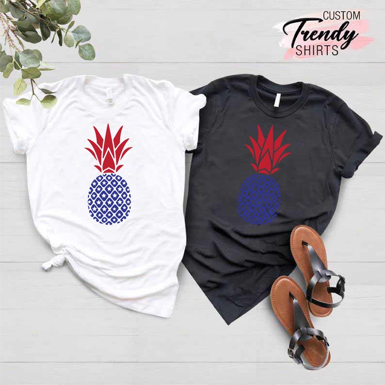 May include: Two t-shirts with a pineapple design. The pineapple is red, white, and blue. One shirt is white and the other is black. CUSTOM Trendy SHIRTS is written in pink at the top of the image.