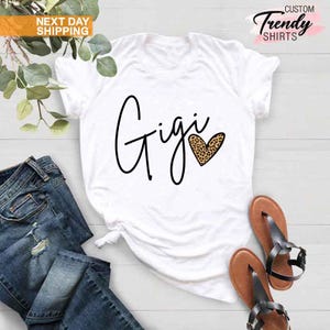 May include: White t-shirt with the word "Gigi" written in black cursive script and a leopard print heart.