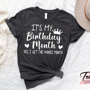 May include: A dark grey t-shirt with white text that reads "It's My Birthday Month" with a crown and hearts. The text below reads "Yes, I get the whole month."