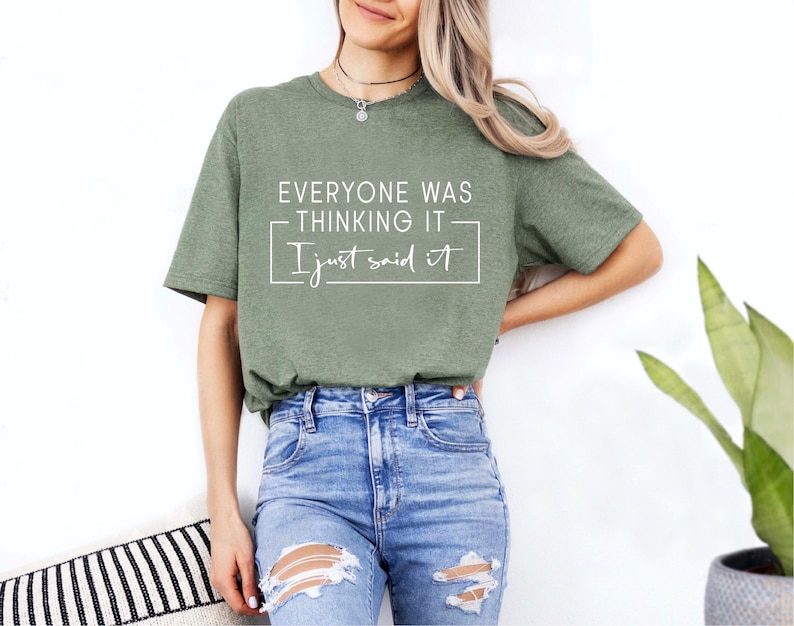 May include: An olive green t-shirt with the text "EVERYONE WAS THINKING IT I just said it" in white. The shirt is paired with blue jeans. The image is of a person wearing the shirt.