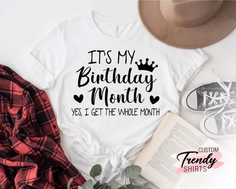 May include: White t-shirt with black text that reads "It's my Birthday Month. Yes, I get the whole month." with a crown and hearts above the text.