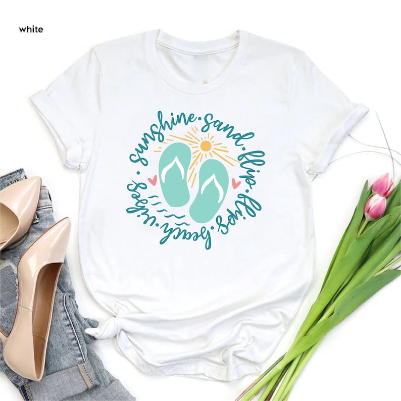 K&ouml;nnte beinhalten: Wei&szlig;es T-Shirt mit einem Grafikdesign von Flip-Flops, einer Sonne und dem Text "Sunshine. Sand. Flip Flops. Beach Vibes."