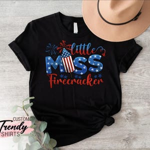 May include: Black t-shirt with a red, white, and blue firework graphic and the text "little miss firecracker".