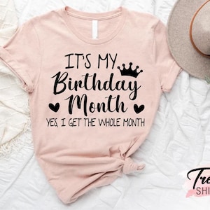 May include: A pink t-shirt with the text "It's my Birthday Month. Yes, I get the whole month." in black lettering. A crown graphic is above the word "Birthday".