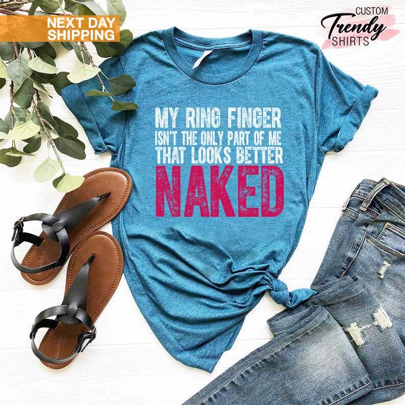 May include: A turquoise t-shirt with the text "MY RING FINGER ISN'T THE ONLY PART OF ME THAT LOOKS BETTER NAKED" in white and pink. The shirt is paired with blue jeans and brown sandals with black straps. The image also includes a sprig of greenery.