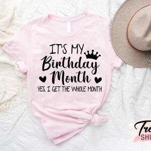 May include: Pink t-shirt with the text "It's My Birthday Month. Yes, I get the whole month." with a crown and hearts.